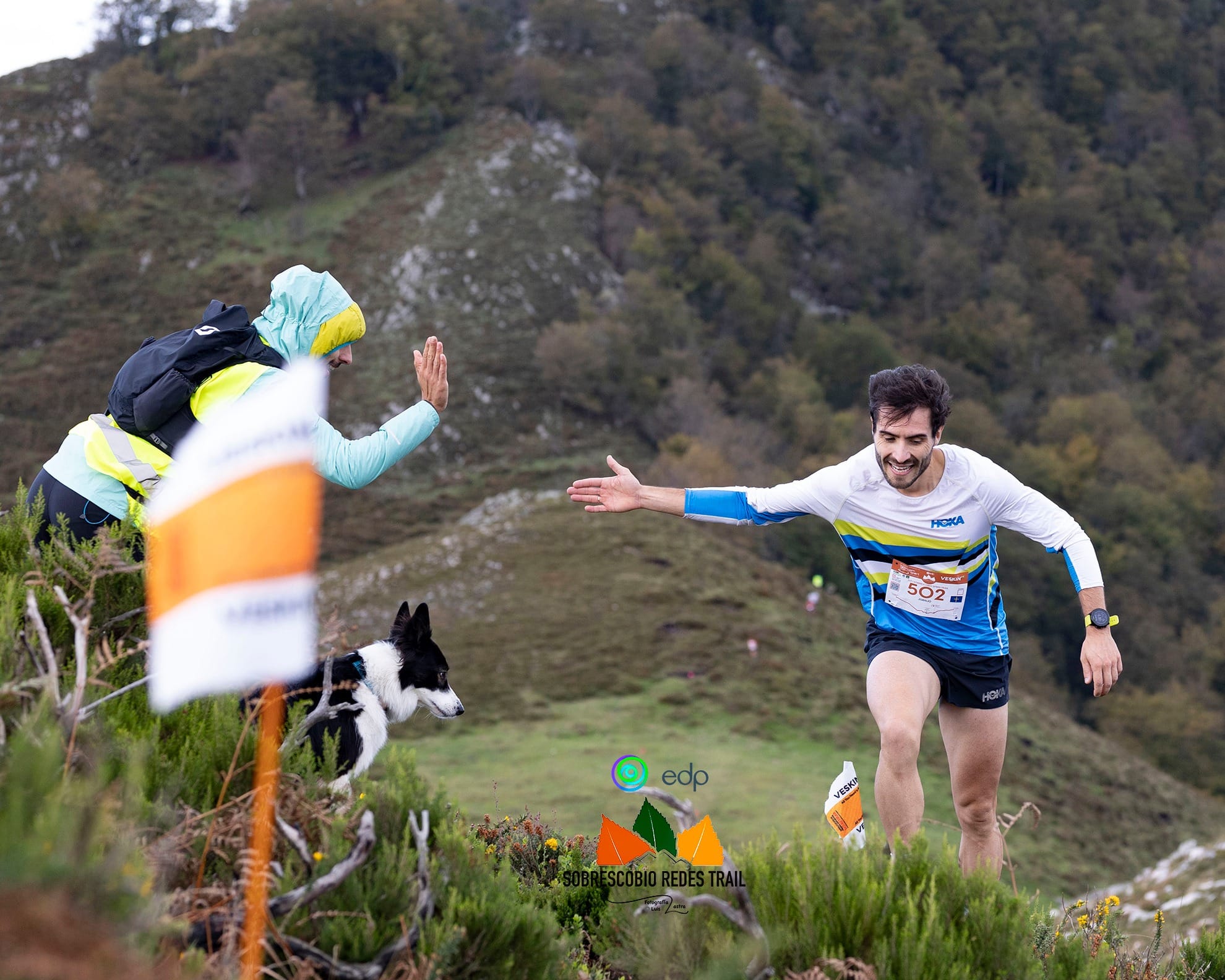 Coureur tapant dans la main d’un spectateur en pleine montée, à côté d’un chien